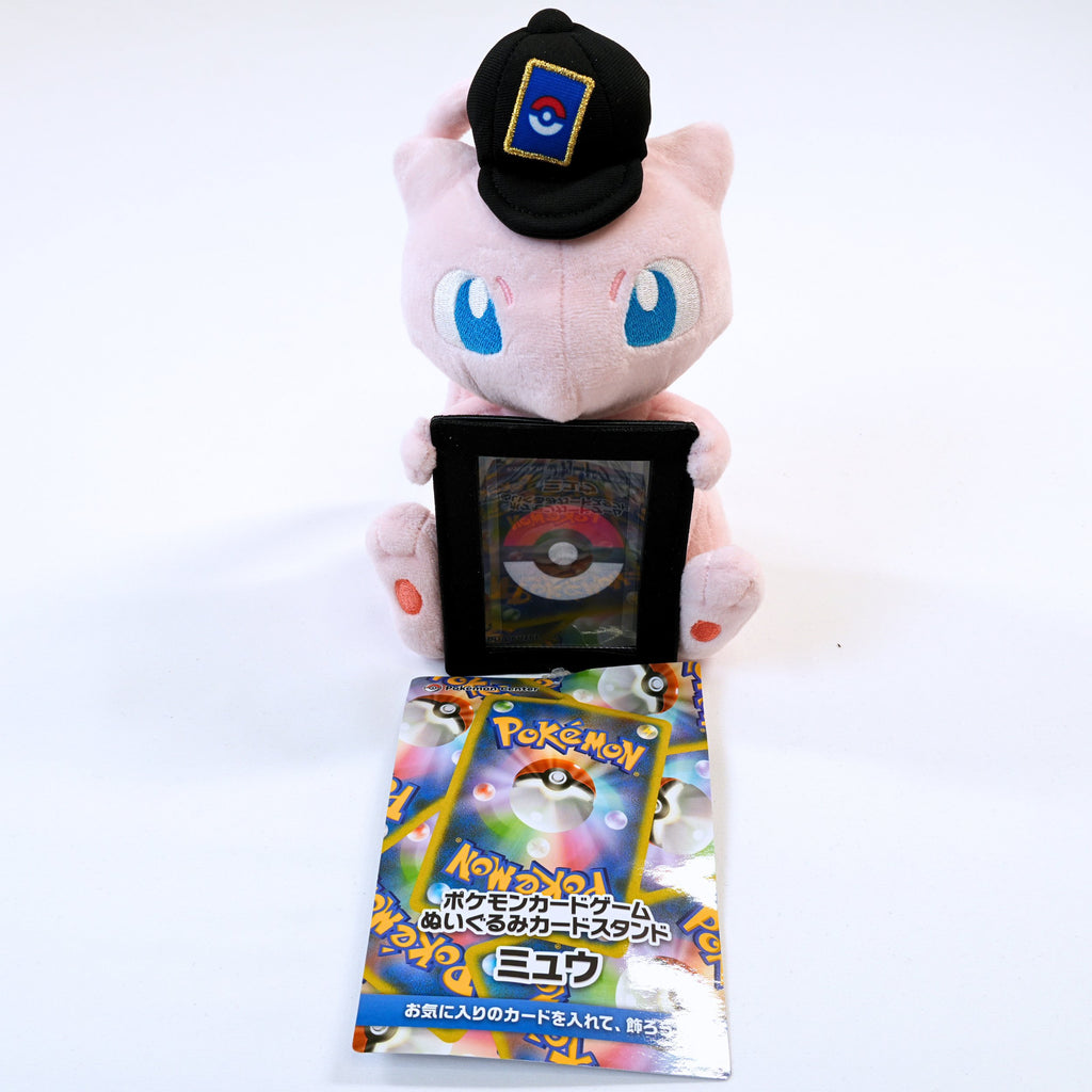 Vista frontal completa del peluche Pokémon Card Stand Mew, mostrando a Mew con gorra y soporte frontal para carta Pokémon junto a la etiqueta japonesa original