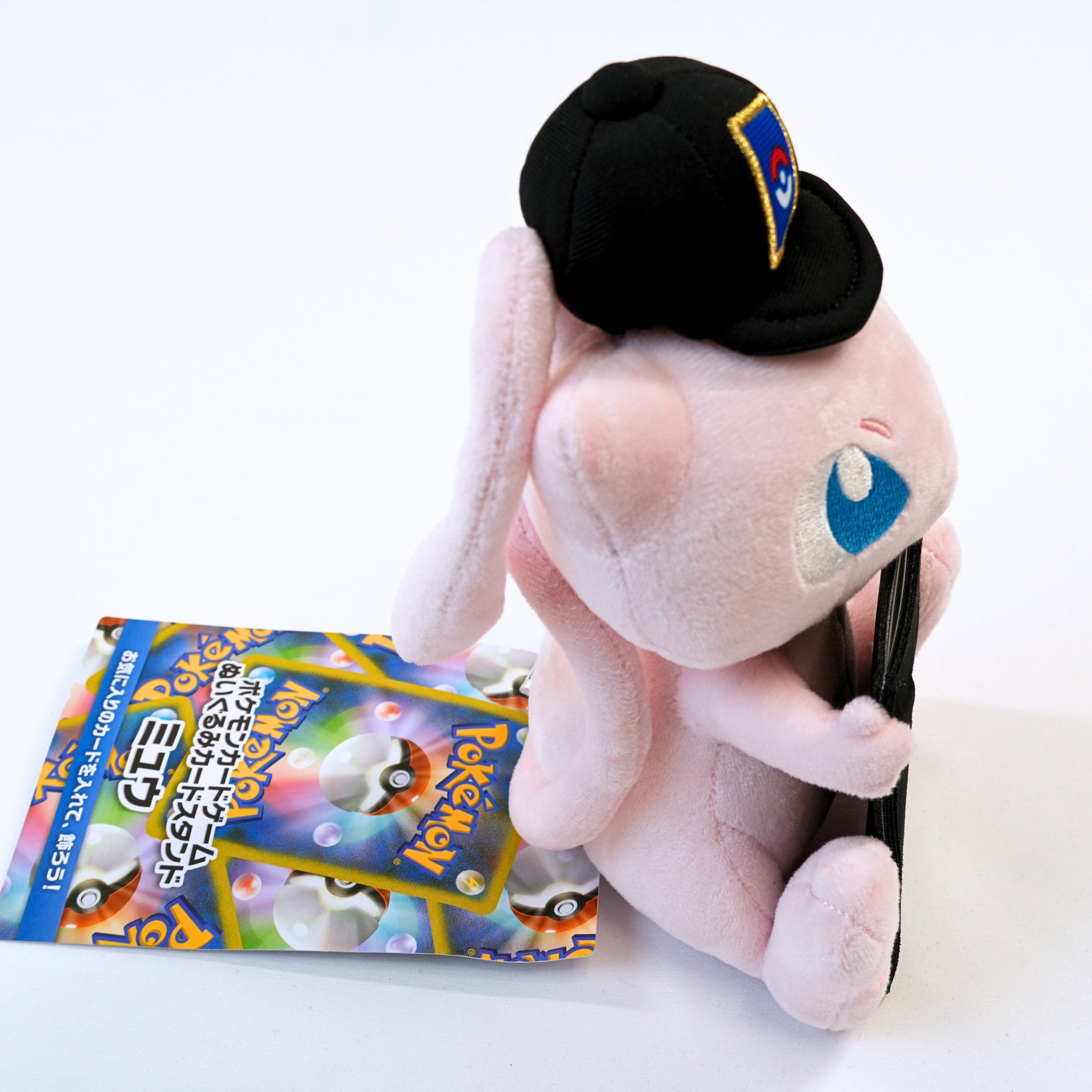 Vista frontal acercada del peluche Pokémon Card Stand Mew, mostrando el detalle de la funda para exponer una carta Pokémon