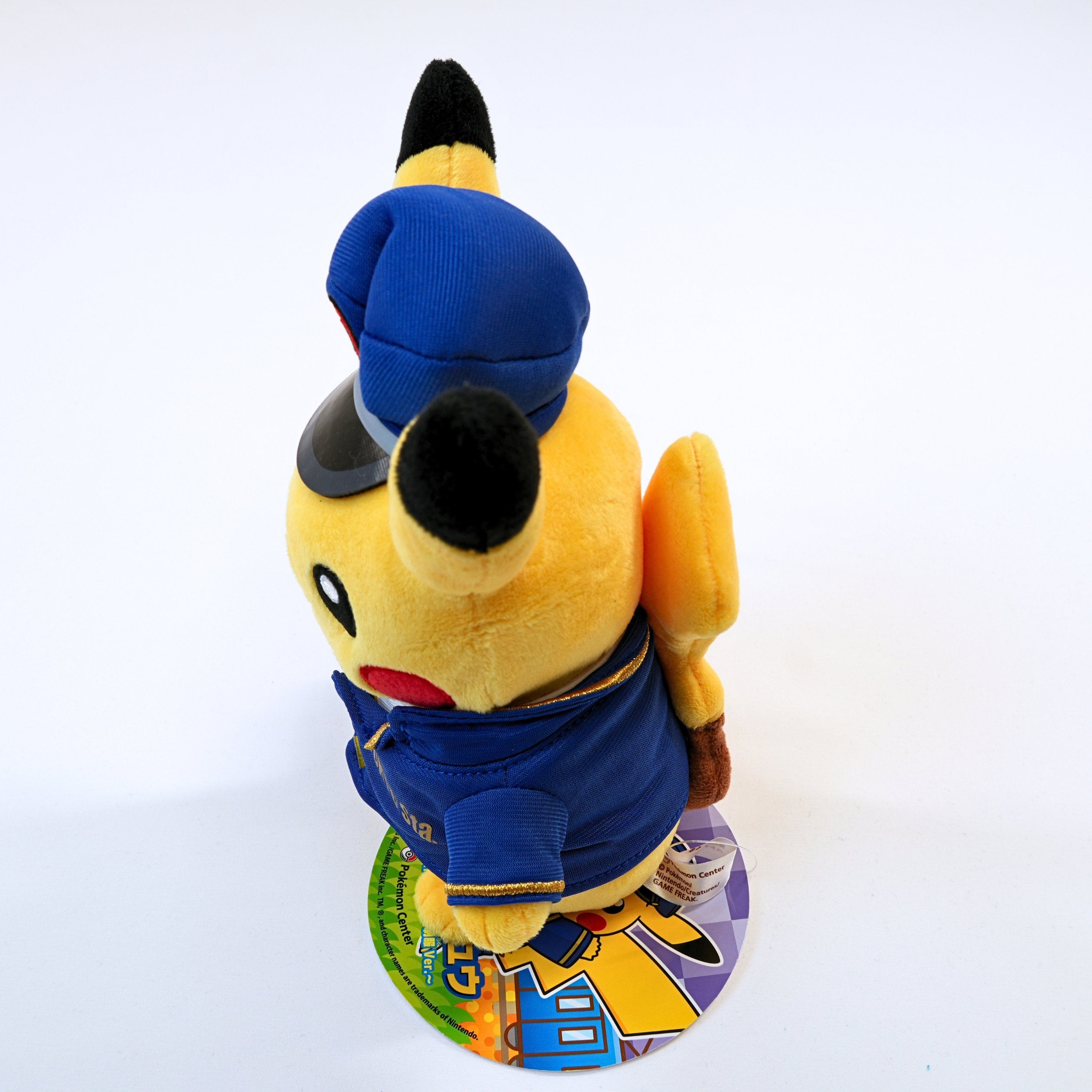 Vista lateral del peluche Pokémon Store Tokyo Station Station Master Pikachu, mostrando el volumen del peluche, el uniforme y los detalles laterales
